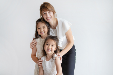 Happy Caucasian mother hugging daughters in pretty outfits and smiling. Two little girls in princess dresses standing together with mother. Joyful family concept.の写真素材