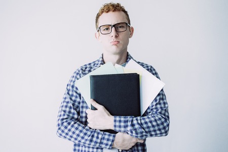 Portrait of young Caucasian redhead male student wearing checked shirt and glasses standing, holding...