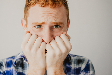 Close-up of frightened face of young Caucasian redhead male student biting nails. Stress and fear conceptの写真素材