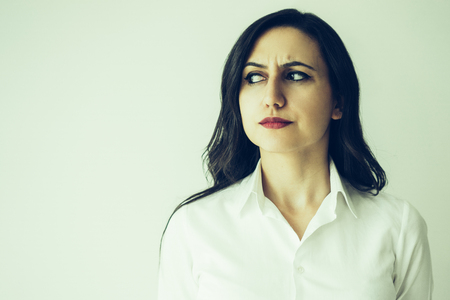 Closeup portrait of suspicious middle-aged beautiful dark-haired woman looking aside and frowning.の写真素材