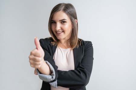 Positive young Caucasian businesswoman showing thumb up. Portrait of pretty dark-haired manager in...