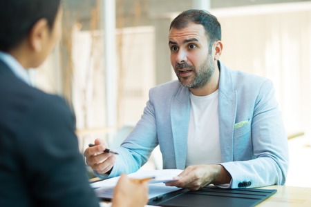 Surprised mid adult male manager talking to female colleague. Latin American manager having meeting with female partner. Meeting and planning conceptの写真素材