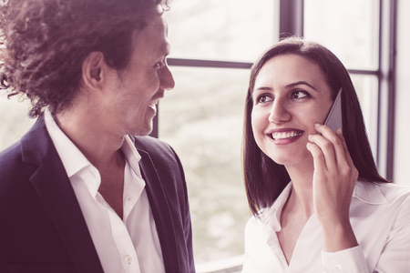 Pretty woman smiling to coworker when calling on phone. Attractive business lady flirting with colleague. Business communication conceptの写真素材