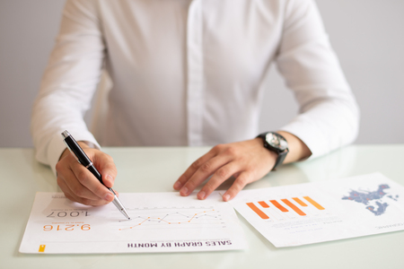 Hands of male manager analyzing marketing report in office. Young Caucasian businessman sitting at table and working with statistic papers. Marketing conceptの写真素材