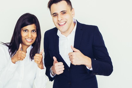 Portrait of happy colleagues, young North American businessman and Indian businesswoman showing thumbs up, looking at camera and smiling. Success conceptの写真素材