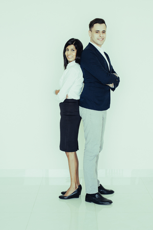 Portrait of successful multiethnic business couple standing together, looking at camera and smiling. Young Indian businesswoman and North American businessman. Team and success conceptの写真素材