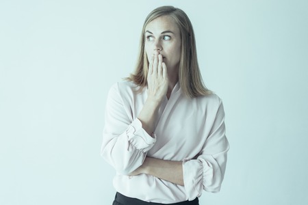 Portrait of young Caucasian woman wearing pink blouse covering mouth afraid to say a word or keeping secret. Secrecy conceptの写真素材