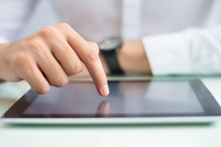 Closeup of person touching tablet computer screen with finger. Man browsing on digital device....
