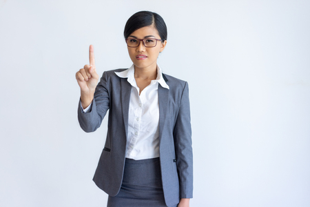 Pensive manager gesturing Brilliant Idea. Beautiful Thai woman in formal suit pointing index finger at copy space upward. Eureka or advertising conceptの写真素材