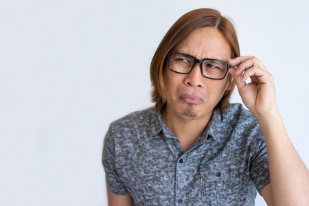 Nerdy Asian guy fooling at camera. Closeup of young man in casual touching eyeglasses, looking away...