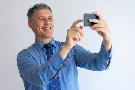 Happy businessman taking selfie. Middle aged Caucasian man in tie having nice video call with phone. Communication and self portrait conceptの写真素材