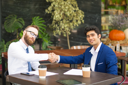 Confident multi-ethnic businessmen shaking hands after signing contract in cafe. Successful business partners congratulating each other with deal. Agreement conceptの写真素材
