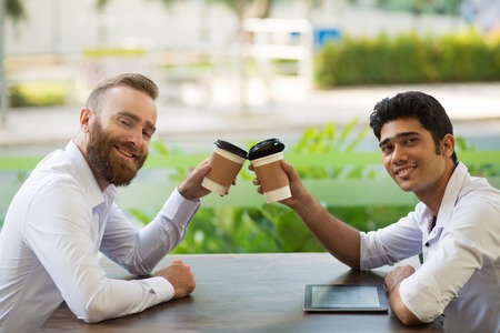 Cheerful business partners toasting with coffee cups while celebrating successful deal in outdoor...