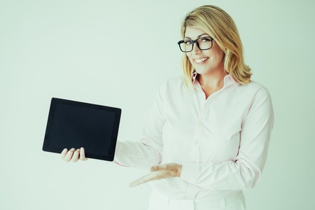 Closeup portrait of smiling middle-aged attractive fair-haired woman holding tablet computer and...