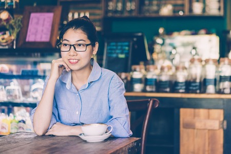 Smiling intelligent girl waiting for order in cafe. Cheerful dreamy attractive young Asian woman enjoying weekend time. Leisure conceptの写真素材
