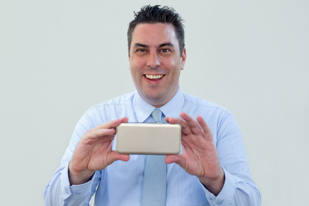 Cheerful handsome businessman shooting video on smartphone and looking at camera. Positive middle-aged man photographing on phone. Technology conceptの写真素材