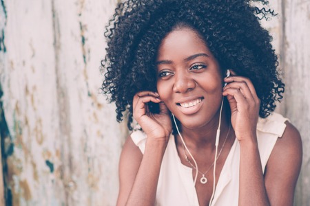 Smiling attractive black woman listening to music outdoors at old wooden wall. Music concept. Front closeup view.の写真素材