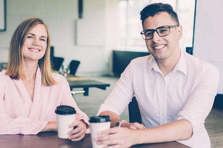 Portrait of cheerful male and female colleagues drinking coffee at break in office. Young Caucasian business people sitting in boardroom and smiling at camera. Coffee break conceptの写真素材