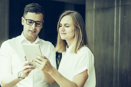 Smiling young colleagues networking on digital tablet. Young Caucasian businesswoman and businessman using touchpad together. Modern technologies conceptの写真素材