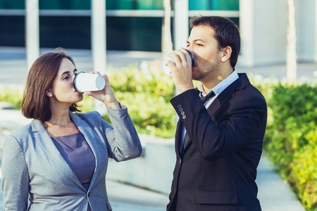 Serious calm business colleagues drinking takeaway coffee outdoors. Pensive content office employee having coffee break. Need more energy conceptの写真素材