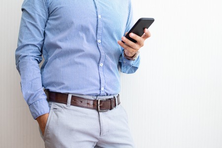 Closeup of entrepreneur texting on smartphone. Man standing and using digital gadget. Technology and communication concept. Cropped front view.の写真素材