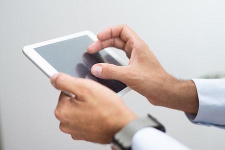 Close-up of man working with online data on tablet. Unrecognizable businessman analyzing information...