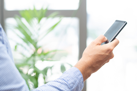 Closeup of business person tapping on smartphone screen. Man texting on digital gadget in office. Technology and communication concept. Cropped side view.の写真素材