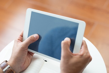 Closeup of man using tablet computer at coffee table. Person browsing on digital device. Technology and communication concept. Cropped view.の写真素材