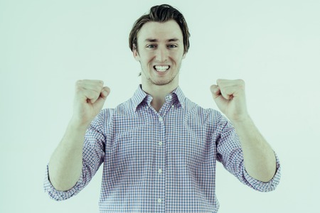 Cheerful young man looking at camera and pumping fists. Success concept. Isolated front view on white background.の写真素材