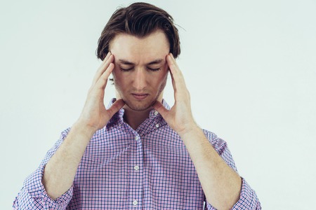 Annoyed young man feeling headache and touching temples. Sad exhausted man in casual shirt keeping...