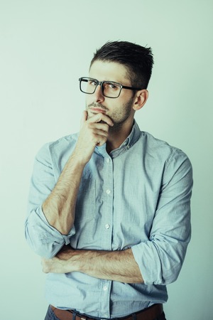 Portrait of pensive young businessman wearing eyeglasses. Caucasian man with hand on chin. Planning...