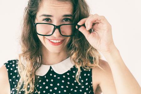 Smiling pretty young woman adjusting glasses and looking at camera over them. Attention concept. Isolated front view on white background.の写真素材