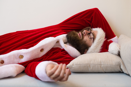 Man wearing Santa costume and sleeping on couch. Bearded guy having rest. Christmas and rest concept.の写真素材