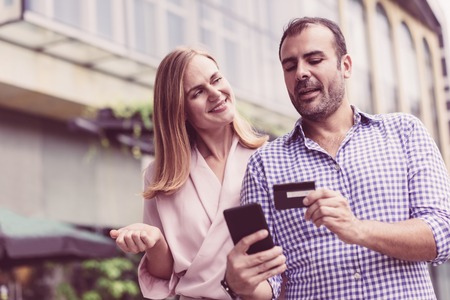 Serious mid adult man explaining to wife how to use online bank. Caucasian couple using credit card and smartphone for online shopping. Online shopping or banking conceptの写真素材