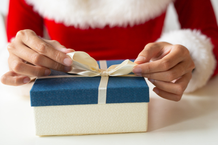 Girl tying ribbon on top of present box. Woman in Santa costume packing gift at desk. Gift wrapping conceptの写真素材