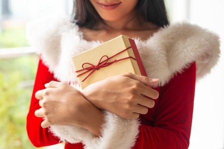 Smiling Christmas girl embracing her gift. Woman in Santa costume holding present box with red bow. Celebration conceptの写真素材