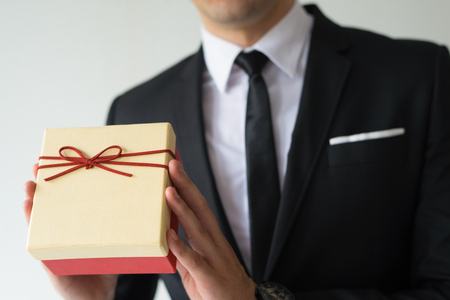 Close-up of businessman in suit presenting Christmas box. Unrecognizable man holding cute yellow box wrapped in thin ribbon. Christmas special offer conceptの写真素材