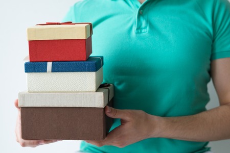 Closeup of guy holding three stacked gift boxes. Person wearing polo t-shirt. Gifts concept. Isolated cropped front view on white background.の写真素材