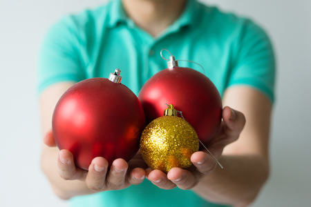 Closeup of guy holding golden and red Christmas balls on palms. Man celebrating Christmas. Christmas party concept. Isolated front view on white background.の写真素材