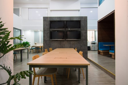 Plasma displays hanging on granite wall in coworking space of modern office. Long wooden table and...