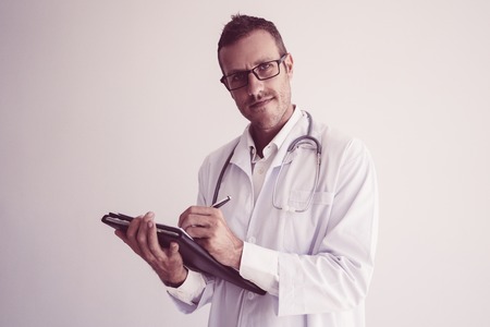 Positive confident doctor filling in medical history cards. Serious male physician in glasses and white coat working with documents. Medicine and recording conceptの写真素材