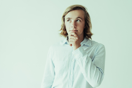 Dreamy young man touching chin and looking away. Attractive guy dreaming. Dream concept. Isolated front view on white background.の写真素材