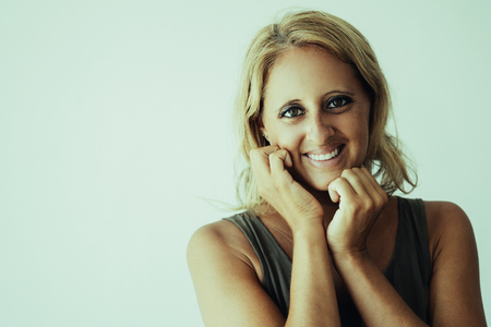 Cheerful blonde lady happy about new cosmetic product and smiling at camera. Closeup of attractive Caucasian woman keeping hands at face and posing. Positive emotions and skin care conceptの写真素材