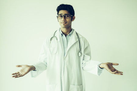 Confused Indian doctor in lab coat expressing misunderstanding. Serious indifferent young clinical worker with stethoscope on neck shrugging shoulders and looking at camera. Puzzlement conceptの写真素材
