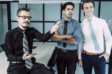 Three business colleagues watching presentation. Mature speaker with tablet pointing hand, his...