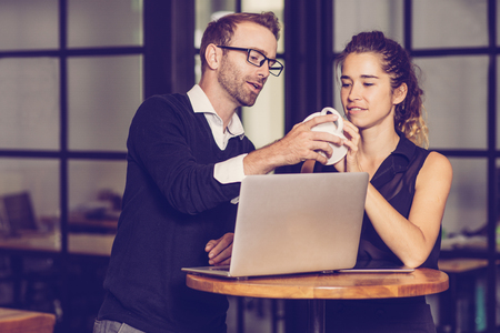 Business partners chatting and working at cafe table. Man and woman using laptop computer, holding cup and looking at it. Business partners concept.の写真素材