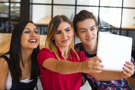 Portrait of happy young friends taking selfie with pc tablet. Two young Caucasian female and one...