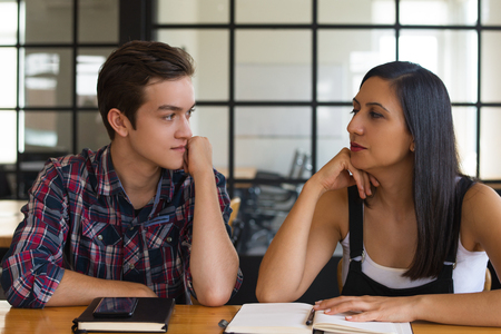 Portrait of young student friends talking in classroom. Caucasian man and woman sitting at table and looking at each other. Relationships and students conceptの写真素材