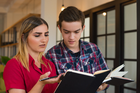 Portrait of serious student boy and girl discussing lecture. Young Caucasian boy and girl reading...