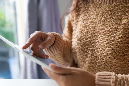Close-up of woman in sweater changing data in online file while using digital tablet. Unrecognizable lady checking information. Data conceptの写真素材